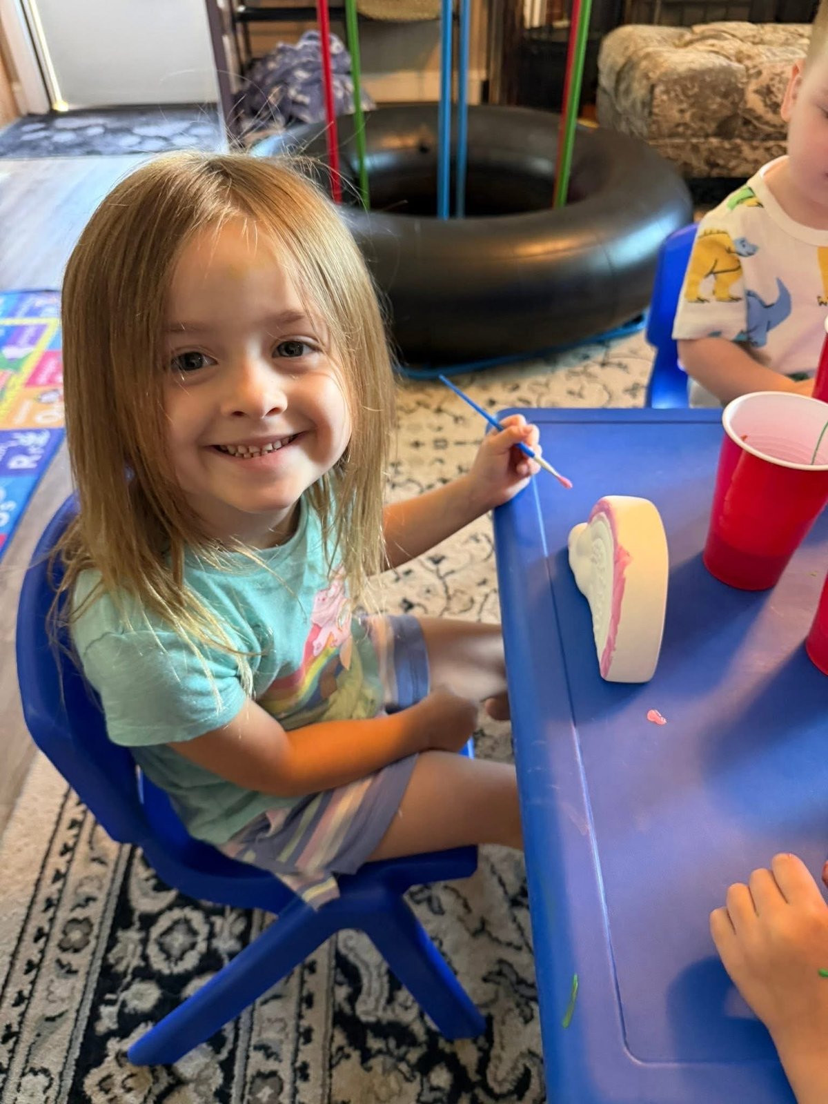 Young smiling child at a blue table during arts and crafts at Mother Goose Day Care