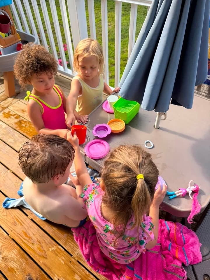 Four young children playing together on a sunny deck at Mother Goose Day Care
